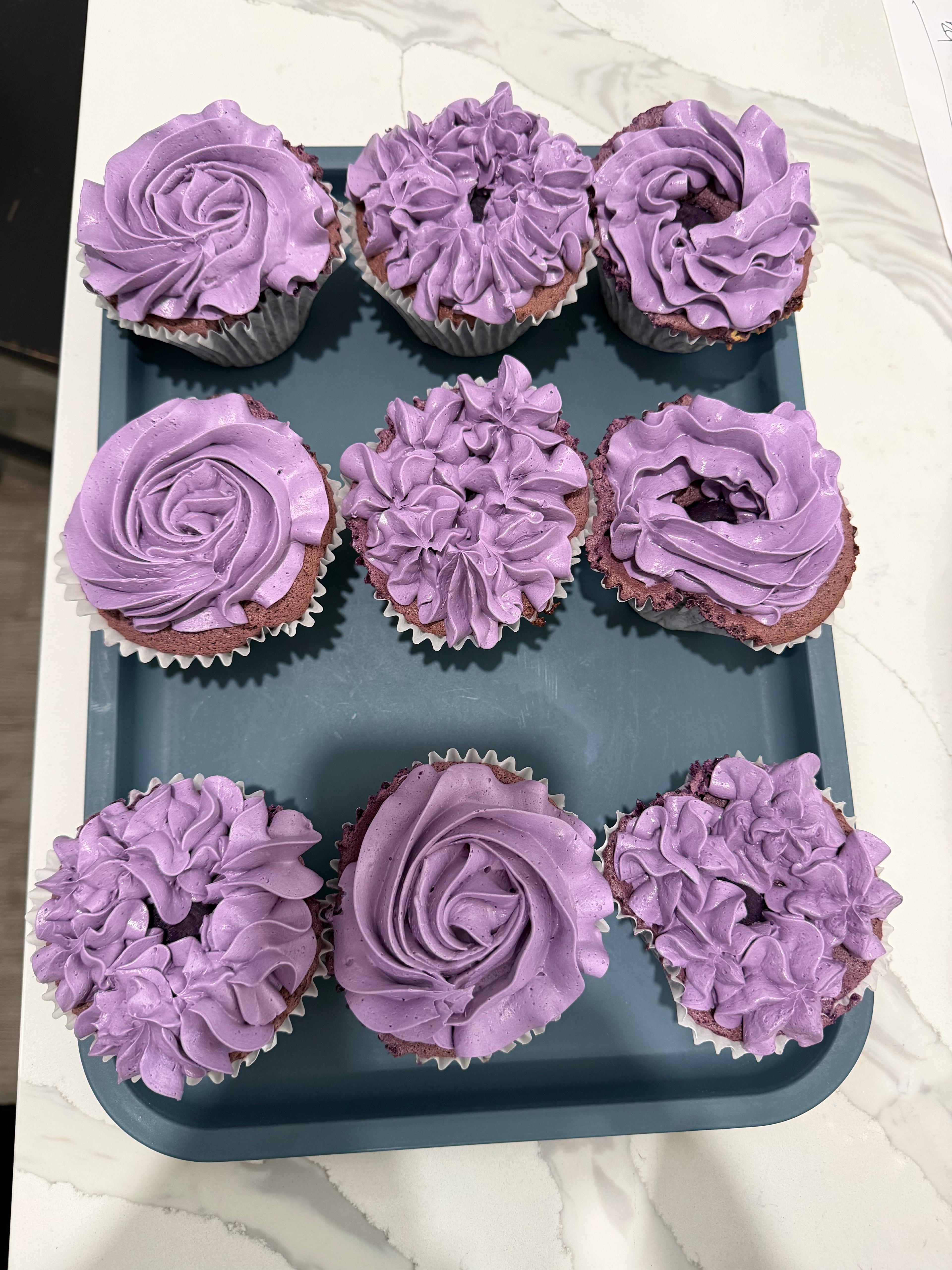 Six purple-frosted cupcakes with piped rose and star swirls