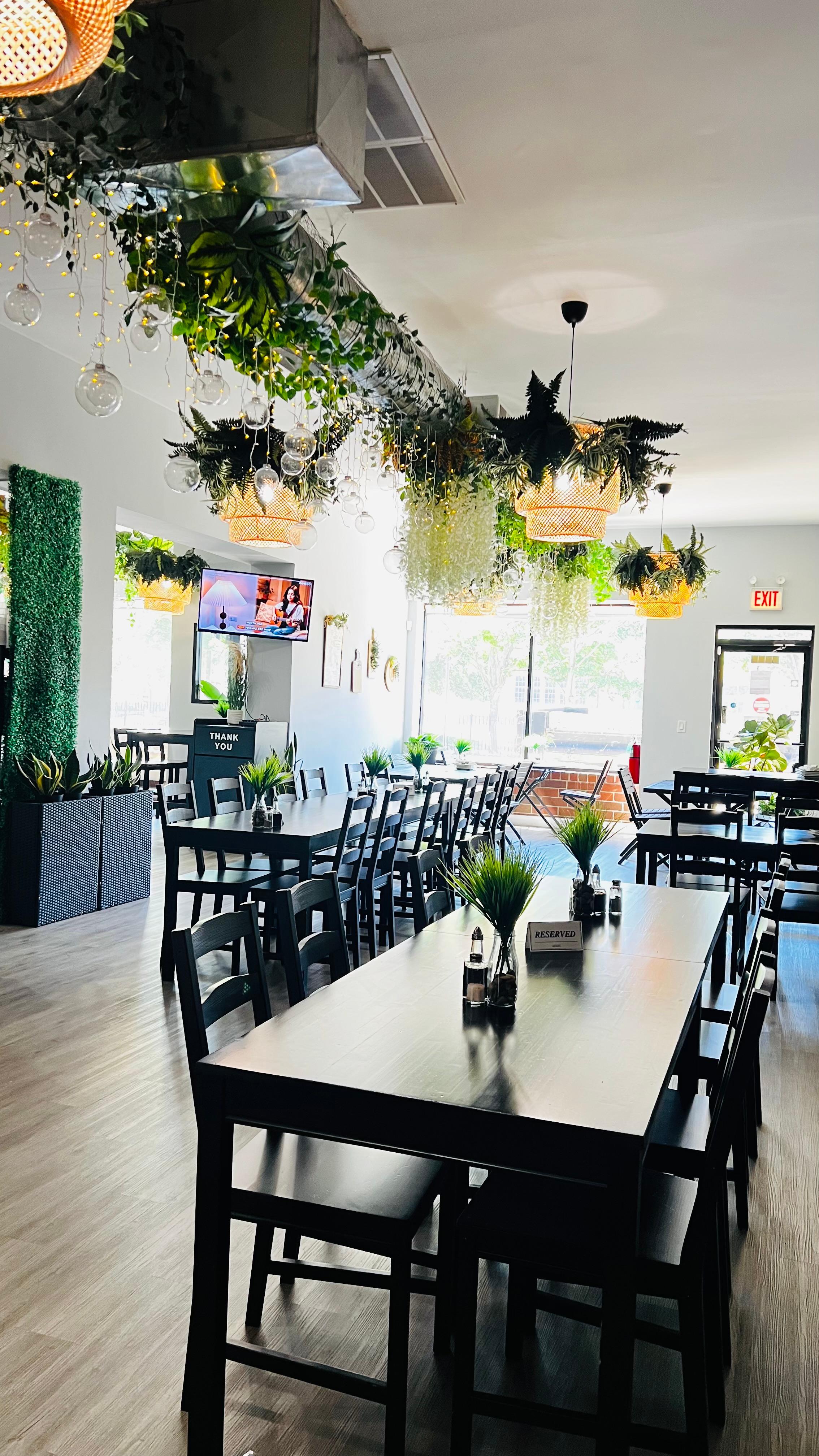Dining room with long communal tables, hanging plants, and wicker lights