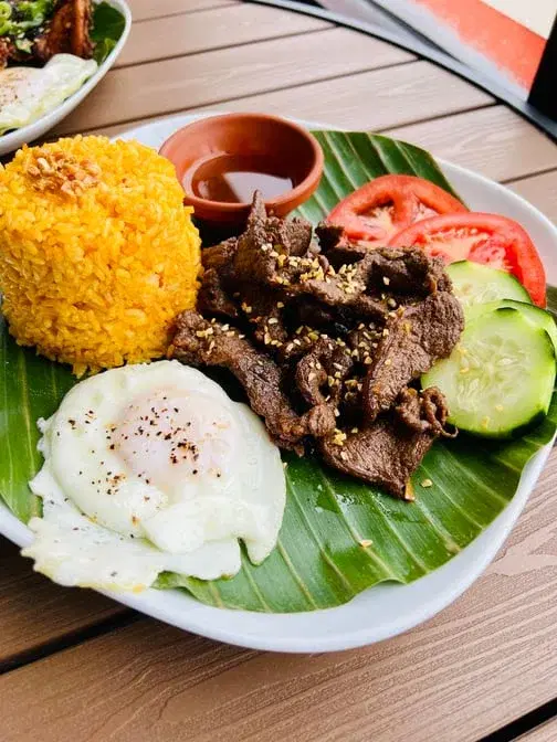Garlic beef strips with fried egg, turmeric rice, cucumber and tomato slices
