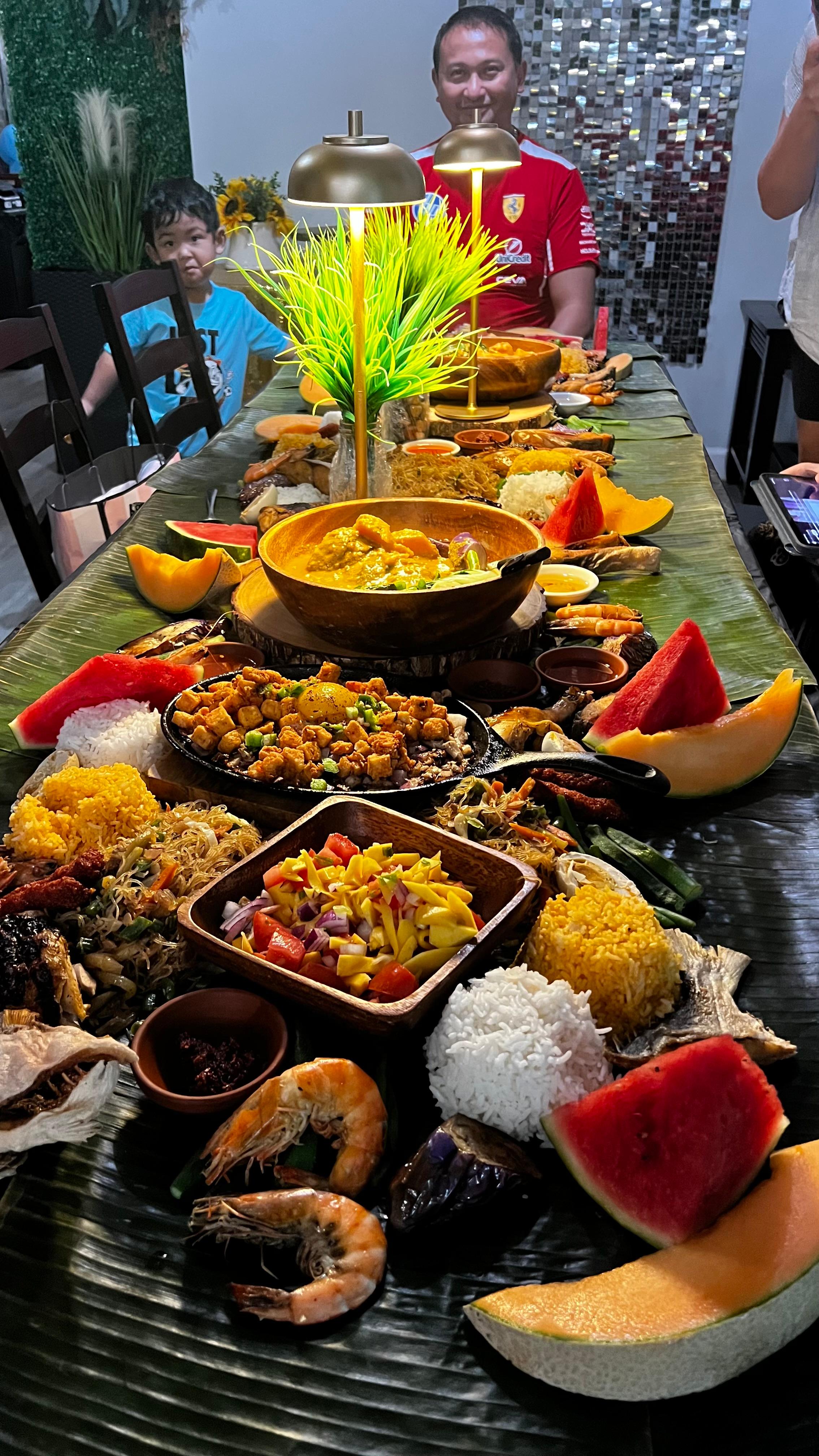 Long communal Filipino boodle feast with rice, prawns, grilled fish, fruits